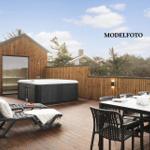 Terrasse mit Whirlpool, Liegestühlen und Esstisch. Hintergrund: Holzhaus und Zaun.