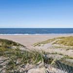 Strand mit Dünen und Windkraftanlagen im Hintergrund.