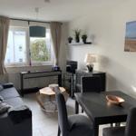 Wohnzimmer mit Sofa, Esstisch und Fenster. Wandbild zeigt Strand.