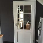 Weiße Tür mit Glasfenstern führt in einen Raum mit Kleiderschrank und Holzbox.