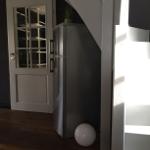 Küchenbereich mit Kühlschrank, Tür und Pflanze unter Treppe.