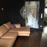 Ein Wohnzimmer mit braunem Sofa, dunkler Wand und Glasleuchte.