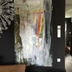 Großes abstraktes Gemälde an schwarzer Wand. Glasleuchte und brauner Sitzbereich.