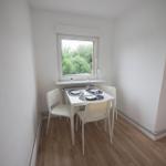 Essbereich mit weißem Tisch und Stühlen, Fenster mit Blick auf Grün.