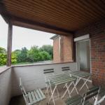 Terrasse mit Tisch und Stühlen, Blick auf grüne Bäume und roten Backsteinbau.