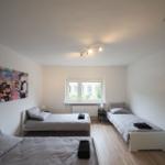 Zimmer mit drei Betten, Fenster und Wandbild.