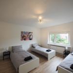 Zimmer mit drei Einzelbetten, Fenster und Wandbild.