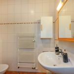 Badezimmer mit Waschbecken, Spiegel, Toilette und Heizkörper.