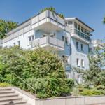 Ein hellblauer Mehrfamilienhaus mit Balkonen und grüner Umgebung.