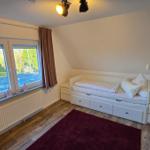 Schlafzimmer mit Dachschrägen, weißem Bett und Holzboden. Fenster mit braunen Vorhängen.