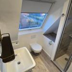 Badezimmer mit Dusche, WC und Waschbecken unter Dachfenster.