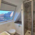 Badezimmer mit Dusche, Toilette und Dachfenster mit Blick auf die Umgebung.
