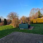 Hinterhof mit Rasen, Steinplatten und Gartenmöbeln. Blick auf Bäume und Nachbarhaus.