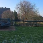 Hinterhof mit Rasenfläche, Terrasse und Gartenzaun. Gartenmöbel sind zugedeckt.