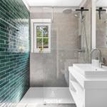 Badezimmer mit Dusche, Waschbecken und grünen Fliesen an der Wand.