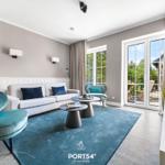 Wohnzimmer mit Sofa, Sessel und Terrasse. Blaue Teppiche und Vorhänge.