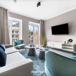 Wohnzimmer mit Sofa, Sesseln, TV und Fenstern zum Balkon.