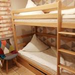 Doppelbett mit Matratzen und Kissen. Wand mit geometrischem Muster. Stuhl mit buntem Sitz.