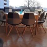 Esstisch mit vier Stühlen vor großem Fenster mit Blick auf Balkon.