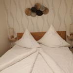 Doppelbett mit weißen Kissen und Decke, Wand mit Muster und Dekoration.