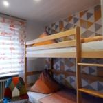 Zimmer mit Doppelstockbett, buntem Stuhl und gemusterter Wand.