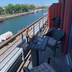 Terrasse mit Tisch, Stühlen und Blick auf Fluss und Boote.