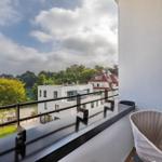 Balcony with modern chair overlooking green park and buildings.