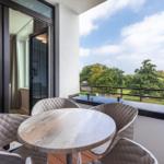 Balcony with table and chairs, view of green trees and sky.