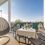 Terrasse mit Tisch, Stühlen und Hängesessel. Blick auf Dächer und Landschaft.