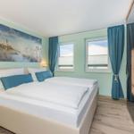 Schlafzimmer mit Doppelbett, Fenstern, Vorhängen und Fernseher.