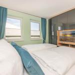 Schlafzimmer mit Doppelbett, zwei Fenstern und TV im Schrank.