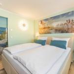 Schlafzimmer mit Bett, Wandbild und Tür zur Strandlandschaft.