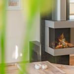 Moderne Wandhalterung mit brennendem Kamin, Holzfußboden und Fenster im Hintergrund.