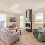 Wohnzimmer mit Sofa, Sessel, Kamin und Fenstern.