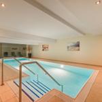 Innere Schwimmhalle mit Pool, Treppe und Pflanzen.