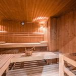 Holzsauna mit mehreren Bänken und einem Eimer mit Löffel.