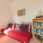 Rotes Sofa mit Kissen, Bücherregal und Segelschiffmodell an der Wand.