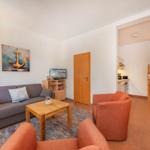 Wohnbereich mit Sofa, zwei Sesseln, Couchtisch und Küchenbereich im Hintergrund.