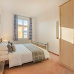 Schlafzimmer mit Bett, Kleiderschrank und Fenster mit Vorhängen.