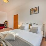 Schlafzimmer mit Doppelbett, Nachttisch und rotem Sofa im Hintergrund.