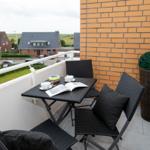 Terrasse mit Tisch, drei Stühlen und Pflanze. Blick auf Wohnhäuser und Grünflächen.