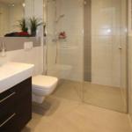 Badezimmer mit Dusche, Waschbecken und Toilette. Rote Handtücher hängen an einem Wärmegerät.