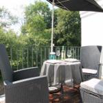 Terrasse mit Tisch, zwei Stühlen und Sonnenschutz. Hintergrund: grüne Bäume.
