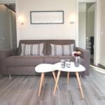 Ein Wohnzimmer mit grauem Sofa, zwei weißen Tischen und Holzboden.