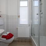 Badezimmer mit Dusche, Toilette und Waschbecken. Fenster mit Jalousie und Heizkörper.