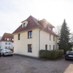 Haus mit rotem Dach und gepflastertem Hof mit parkenden Autos.