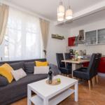 Wohn- und Küchenbereich mit Sofa, Tisch und roten Schränken.