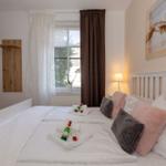 Schlafzimmer mit Bett, Fenster, Wandbild und Flaschen auf Bett.