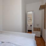 Schlafzimmer mit weißem Bett, Spiegelschrank und Holzgarderobe.