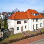 Modernes Haus mit rotem Dach und gepflegtem Garten. Zwei Eingänge und Parkplatz.